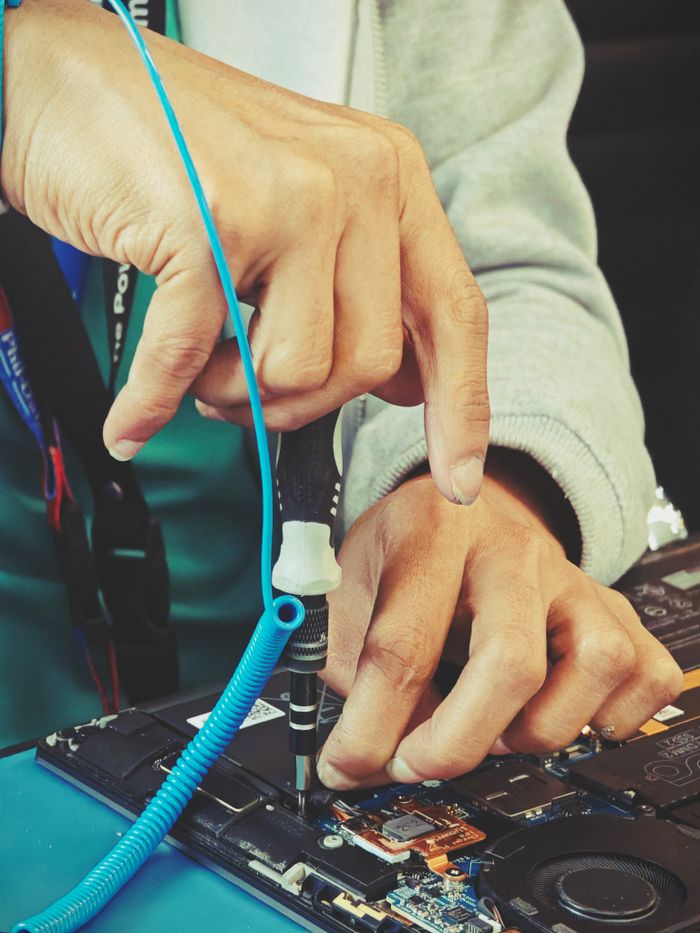 Close-up of a technician's hands repairing a laptop's internal components with tools.